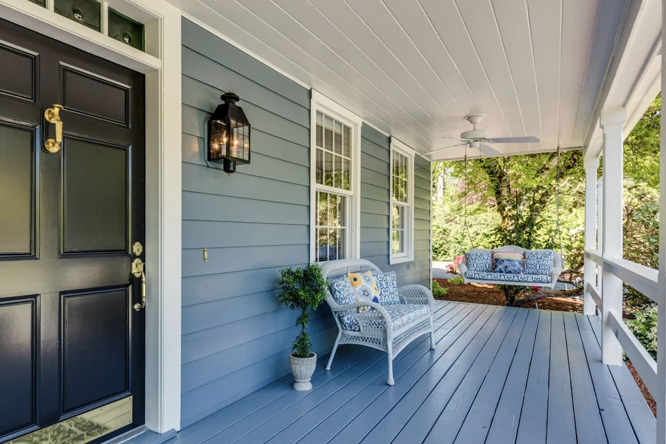 Black paneled front door with a brass knocker beside a covered porch with wicker seating
