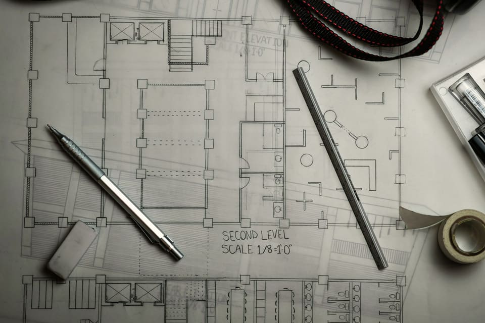 Floor plan drawings spread on a table with a mechanical pencil, a scale ruler and tape