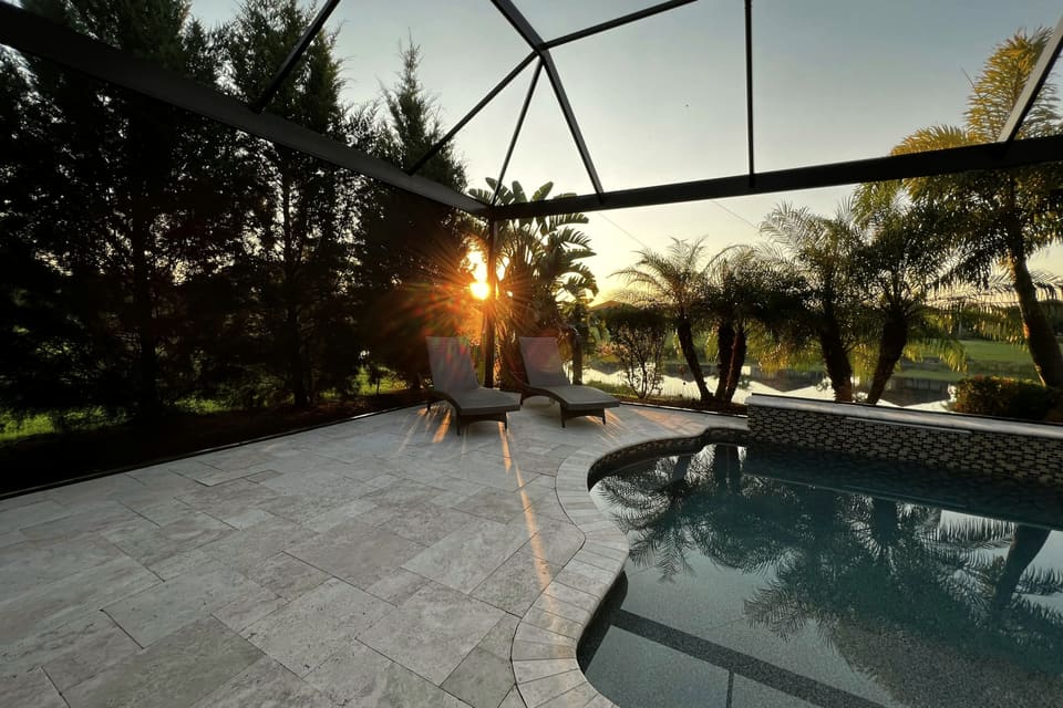 Pool and paver deck inside a screened lanai enclosure, two lounge chairs and palms against a low sun