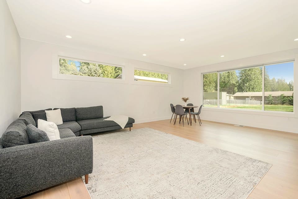 Living room with a gray sectional, a rug on a wood floor and large windows facing a yard