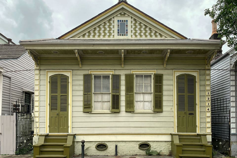 Single-story wood cottage with a pitched gable, louvered shutters and two front doors with steps