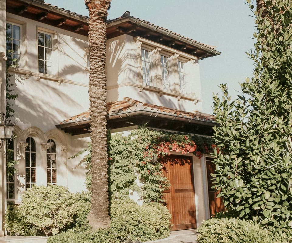 Clay tile roofline over wooden garage doors and climbing bougainvillea, with a palm trunk in front